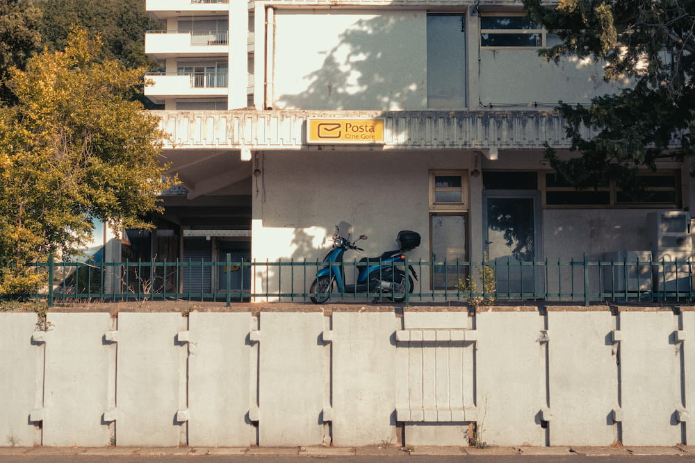A shuttered café behind a white fence, a scooter under the trees