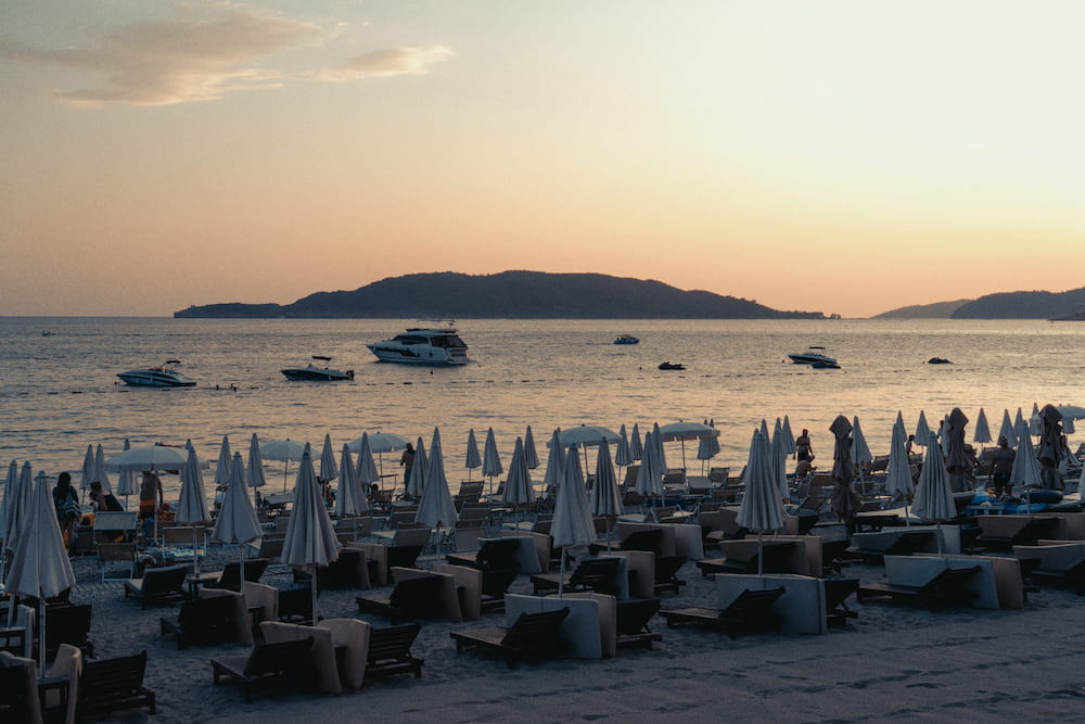 Rows of closed parasols on a beach at sunset, an island offshore