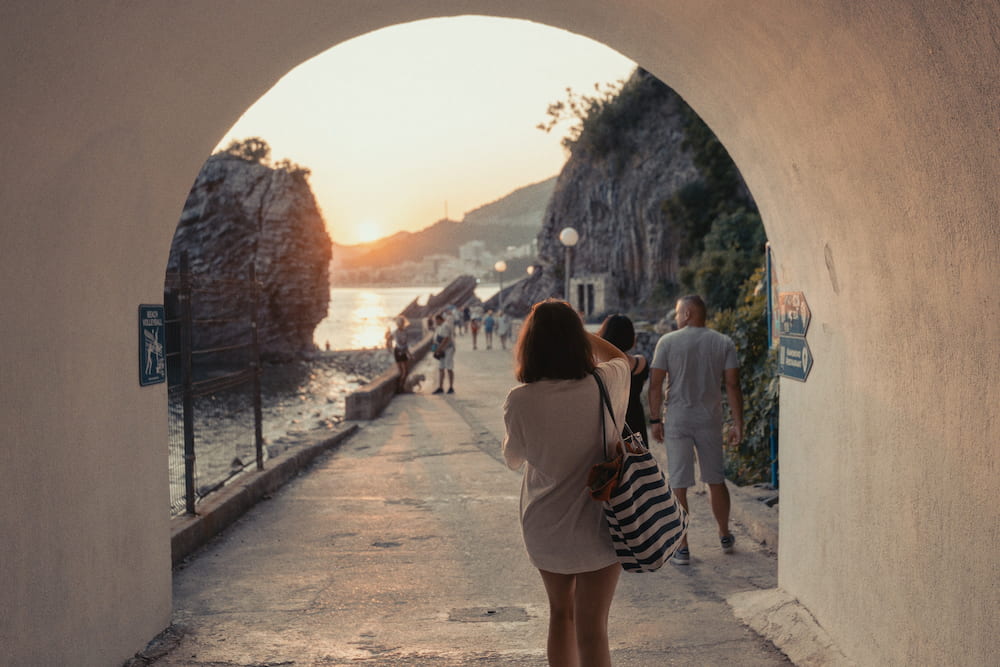 People walking through an arch towards a seafront path at sunset