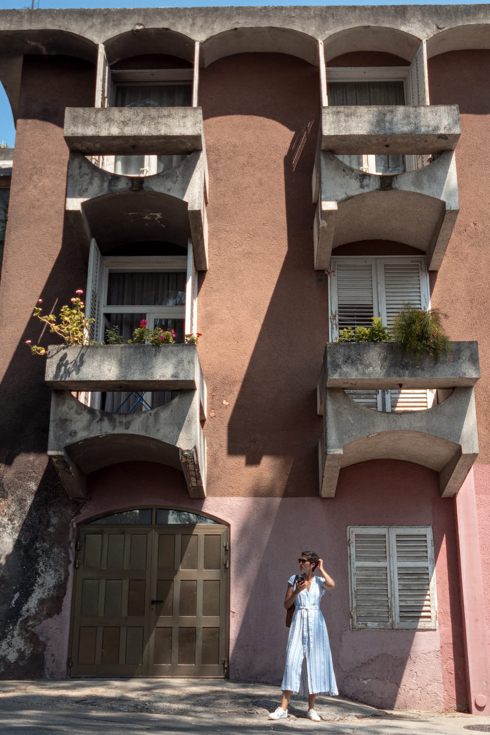 A pink apartment building with balconies, a woman in a blue dress in front