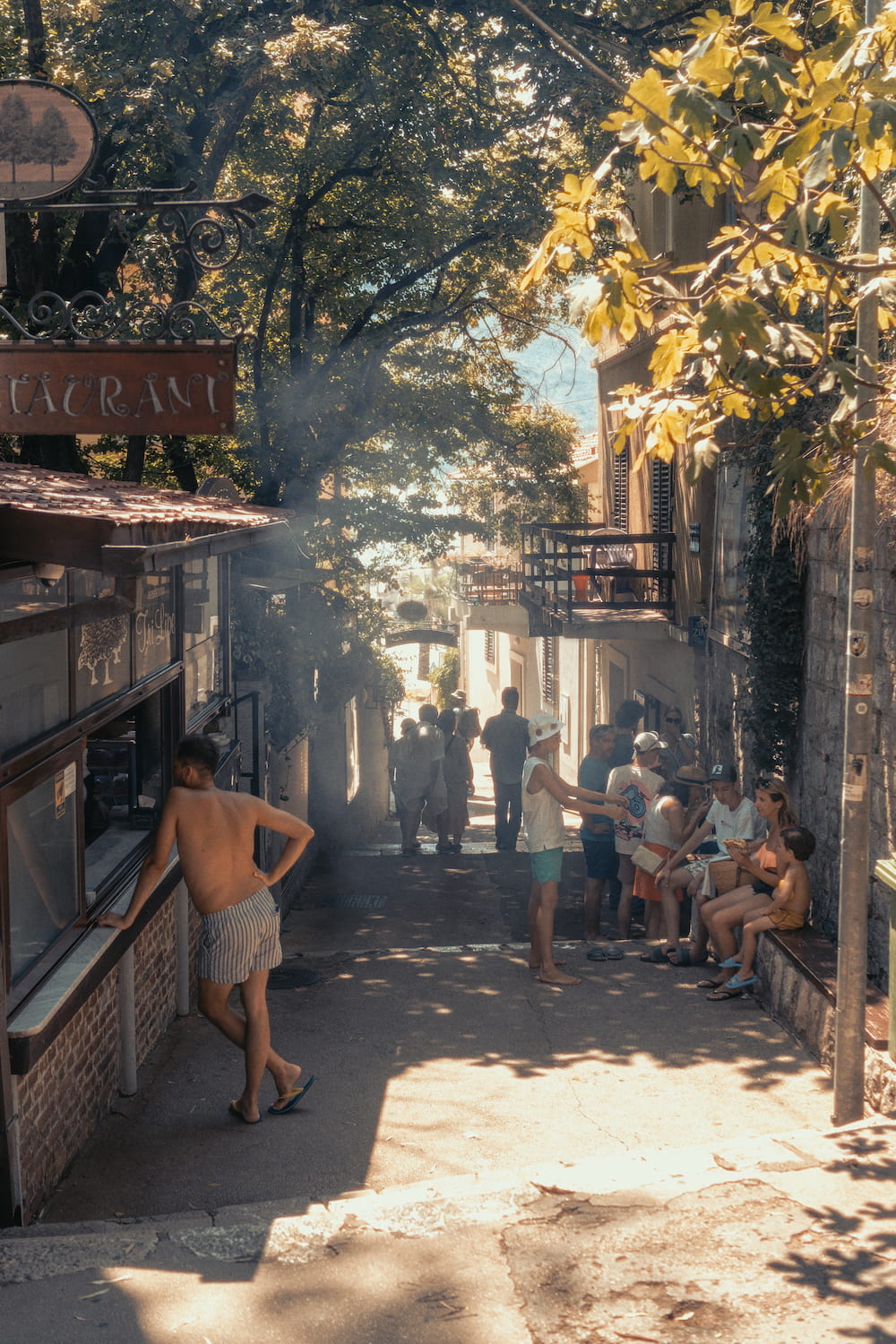 A shaded street with a café, people walking in the sun