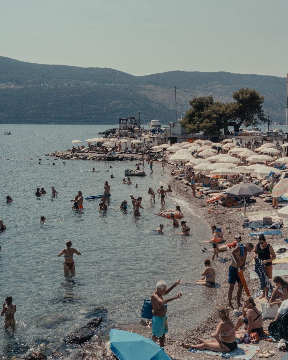 A crowded beach and swimmers, hills across the bay