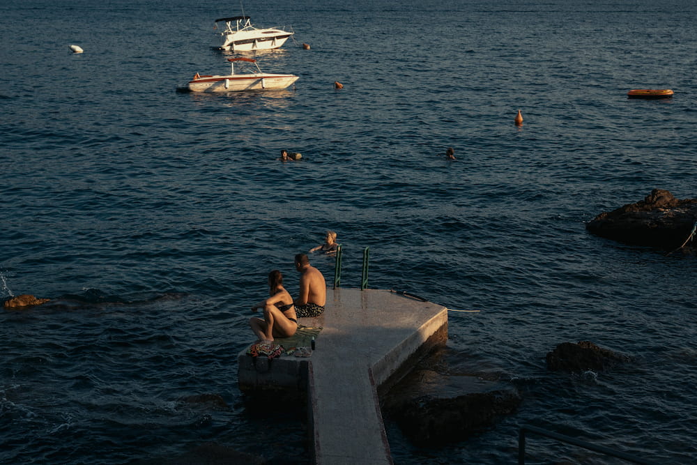 People sitting on a concrete pier among rocks in the bay