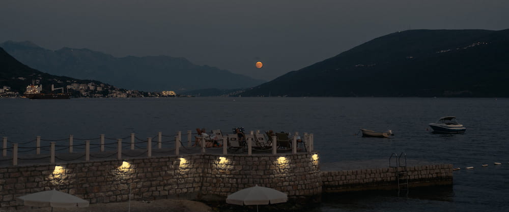 Lights along a stone pier at dusk, hills across the bay