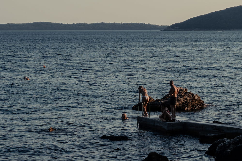 Two people on a rock beside a pier in the evening sea