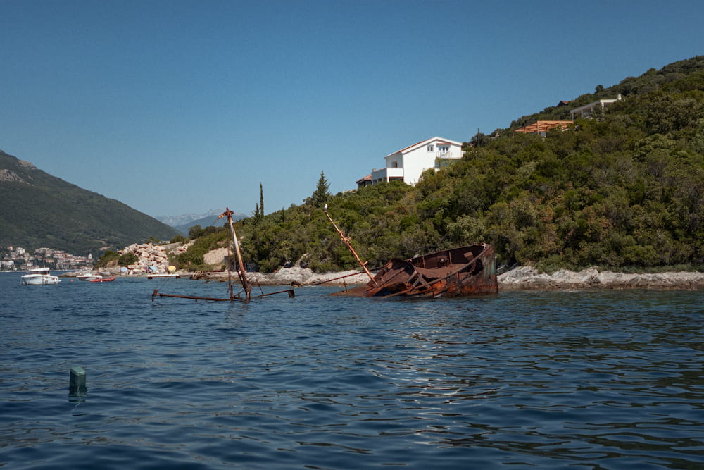 A rusty wreck in a cove below a green hillside