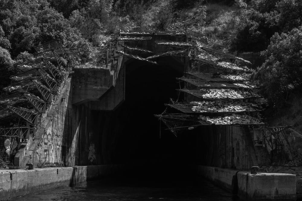 Black and white: a tunnel mouth in the hillside at the water's edge