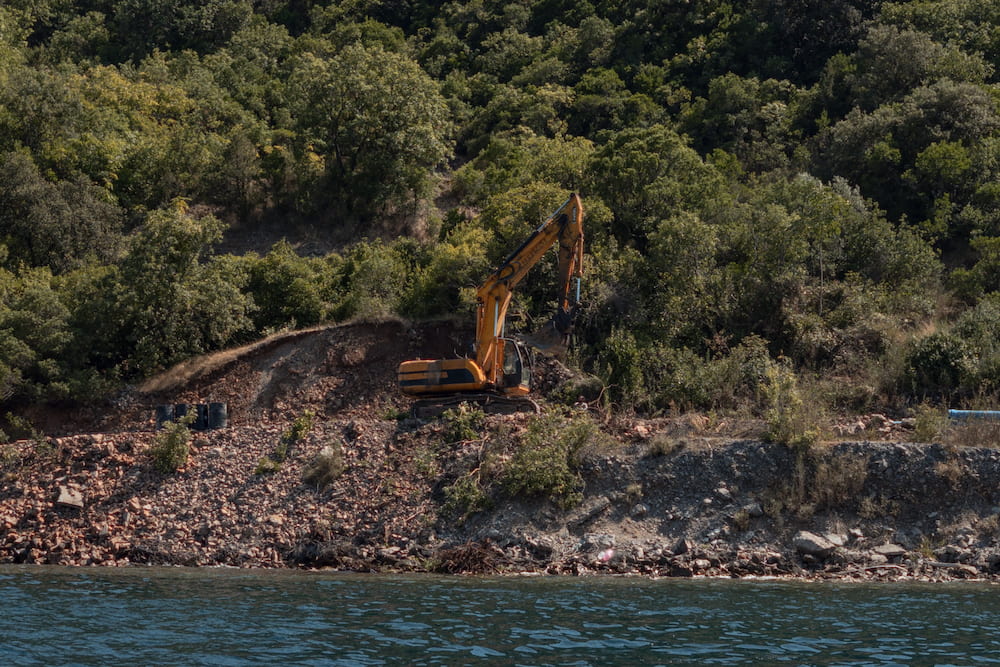 An excavator clearing a wooded slope by the sea