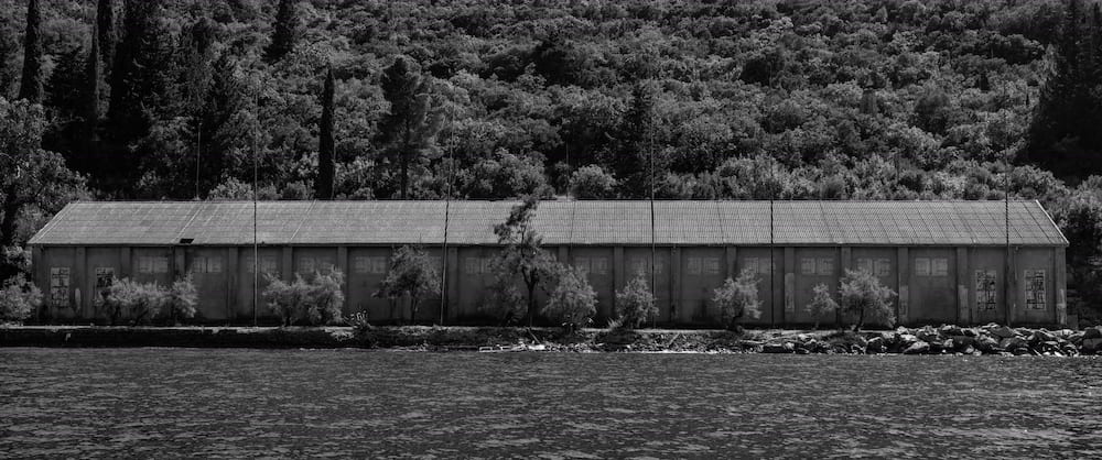 A long shed on the shore under a wooded hill