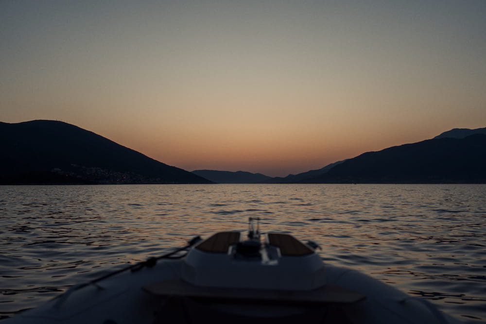 The bow of a boat heading into a sunset between hills