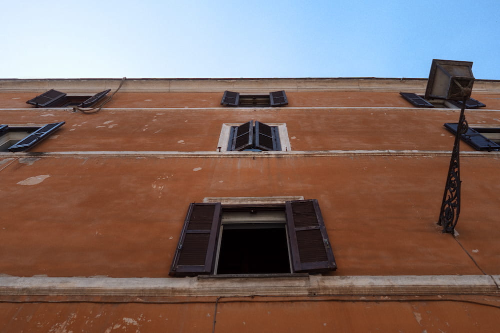 An orange wall with shuttered windows under a blue sky, from below.