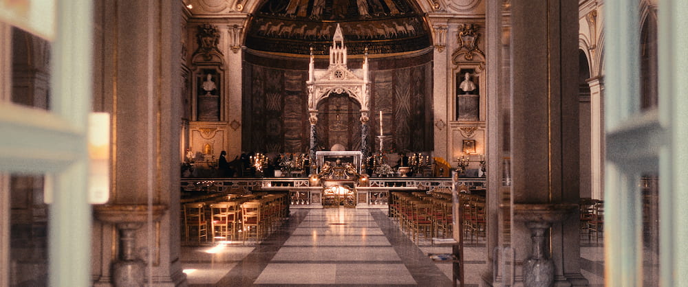 A church nave with a gilded apse and an altar canopy, seen through a doorway.