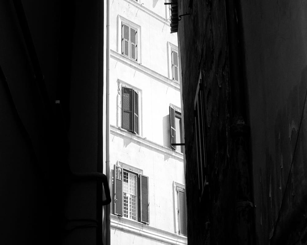 A pale building front in a slot of light between two dark walls.