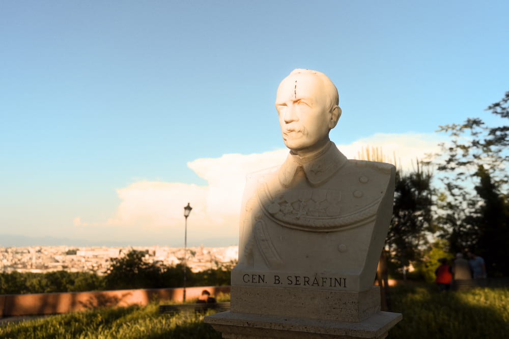 A marble bust against a blue sky, the city below in evening light.