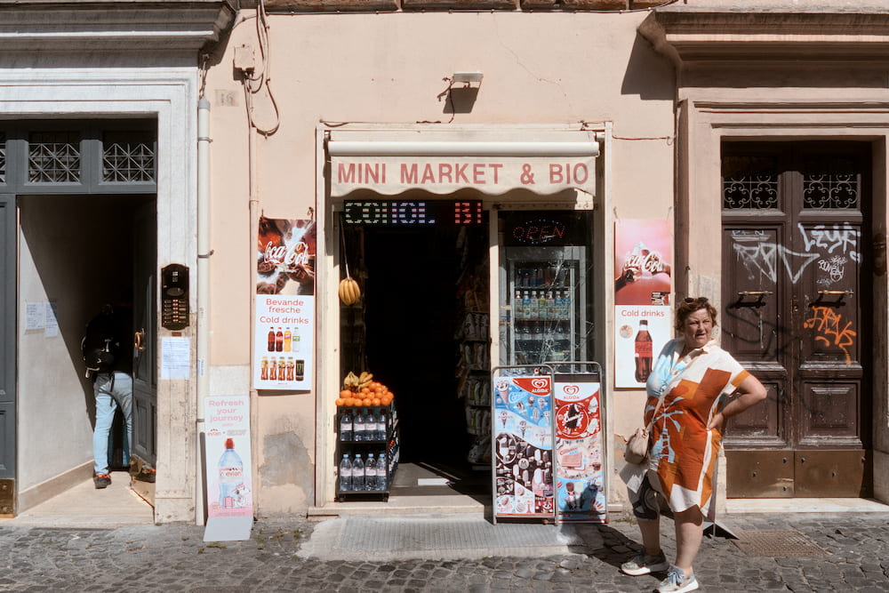 A woman in an orange apron standing outside a mini market.