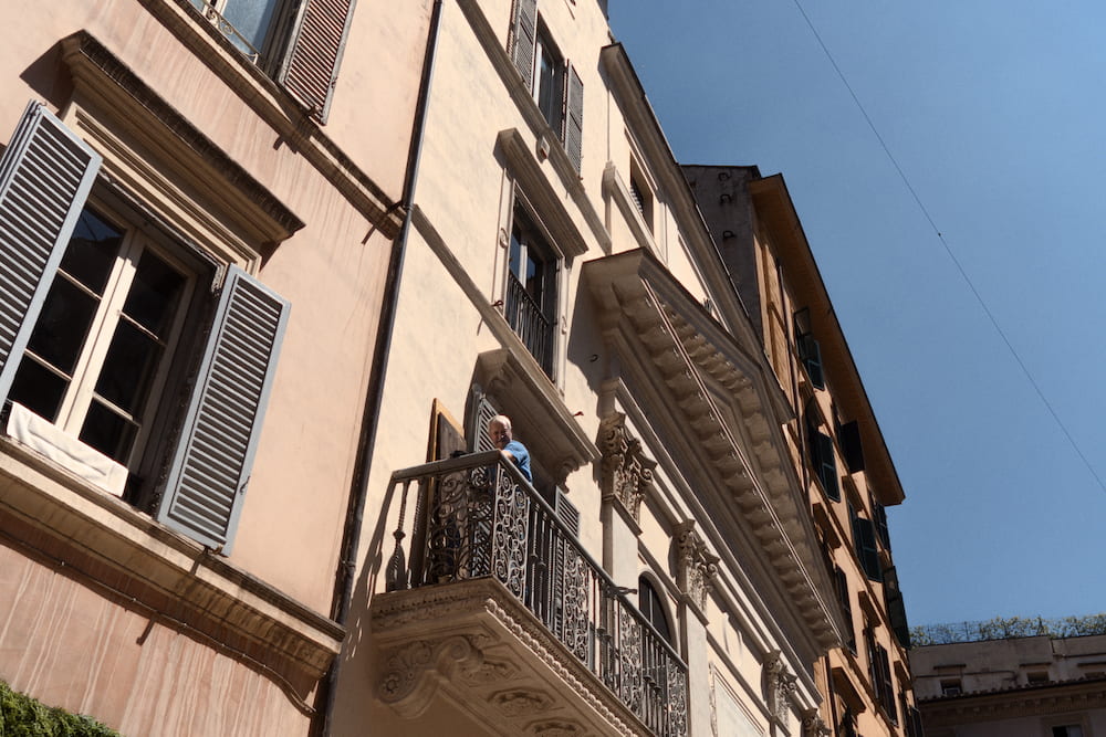 Looking up at a pale building with shutters and a balcony.