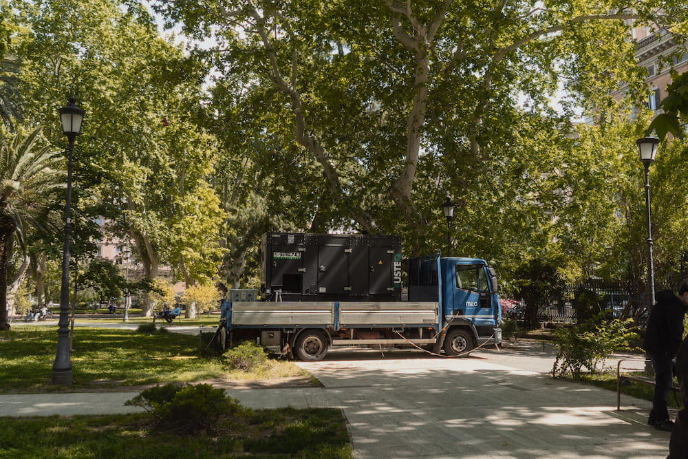 A park path under plane trees, a blue truck parked on it.