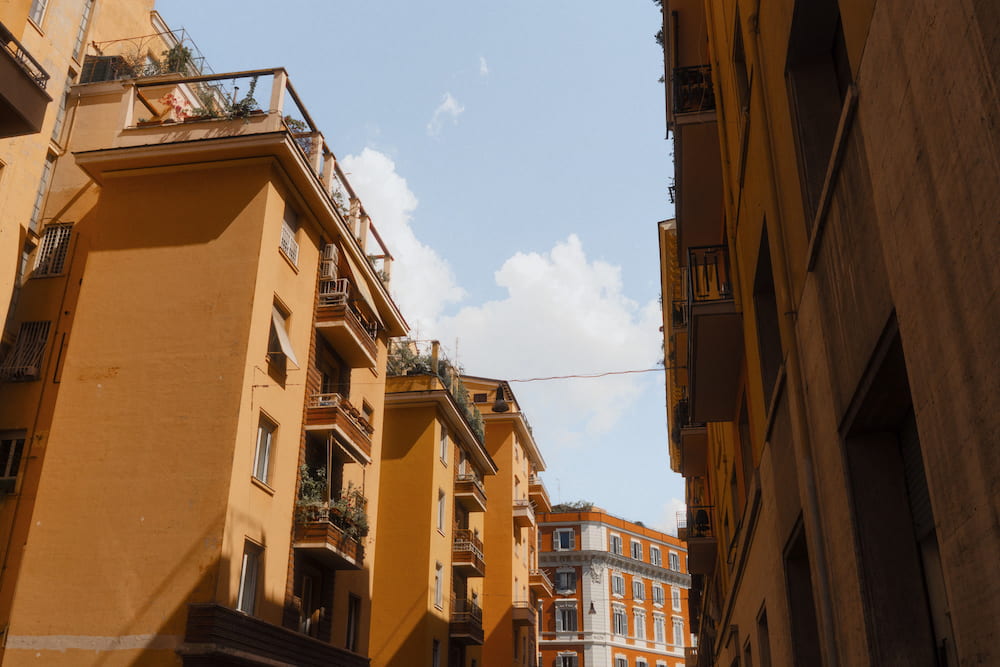 Ochre apartment blocks with balconies against a blue sky, from below.