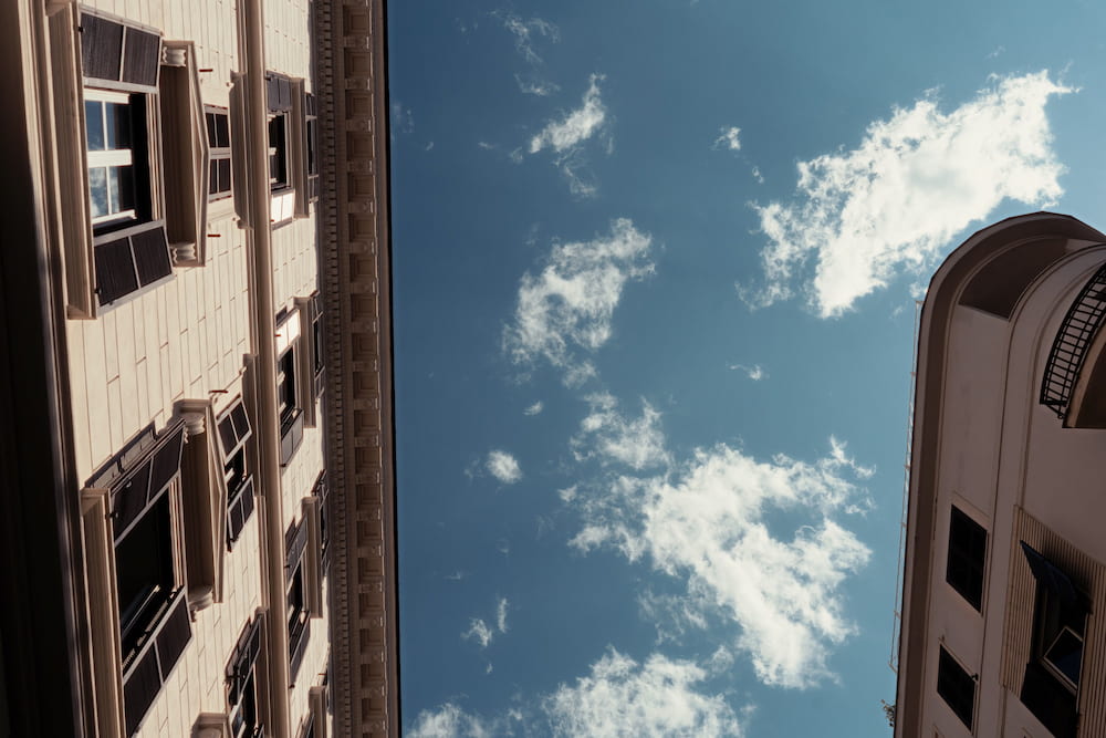 Looking up between building fronts at a blue sky with small clouds.