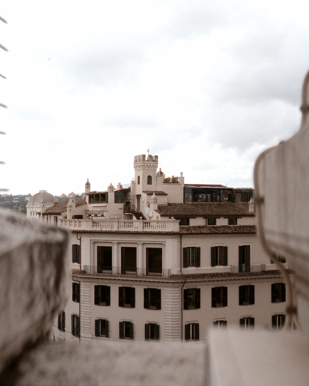 Rooftops and a building seen past a stone ledge, under cloud.