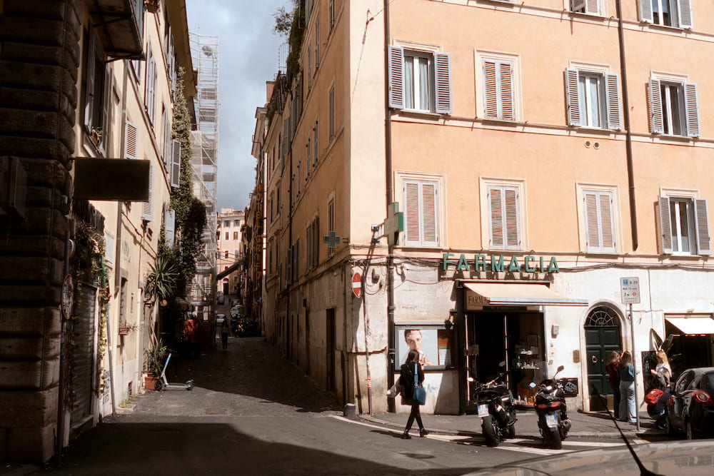 A narrow street of pale ochre houses, people and scooters.