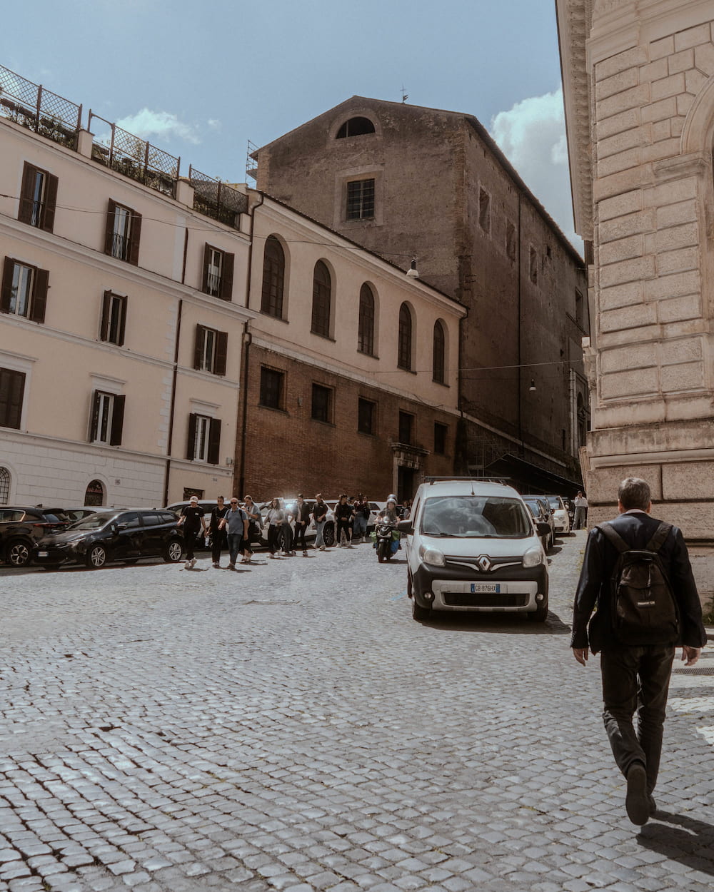 A man with a backpack walking up a cobbled street, a car coming.