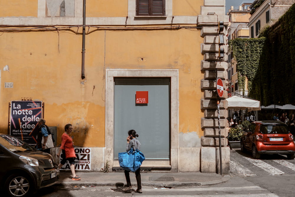 A woman with a phone and a blue bag in front of an ochre wall.