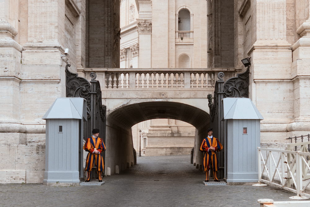 Two Swiss Guards beside sentry boxes at an arched gate.