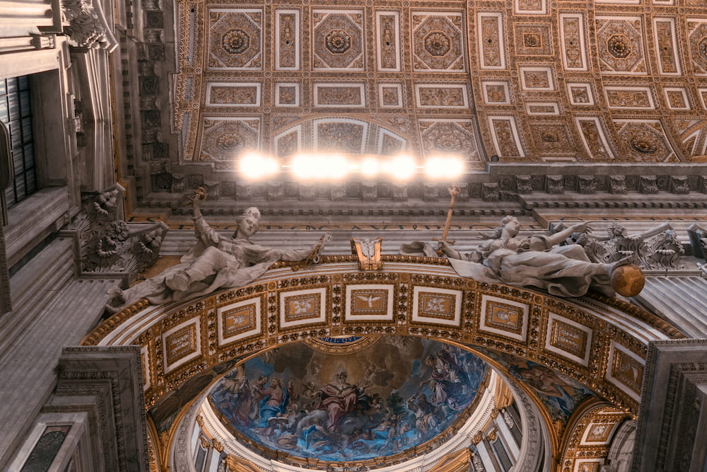 A gilded coffered ceiling with a row of lights inside a basilica.