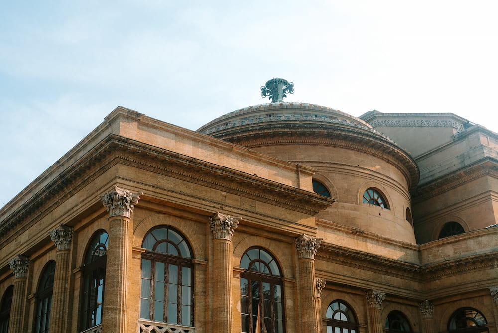 Columns, arched windows and a domed roof of a golden stone building against a pale sky