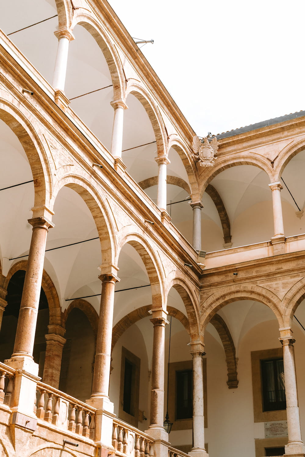 Two storeys of stone arches on slim columns around a courtyard under a white sky