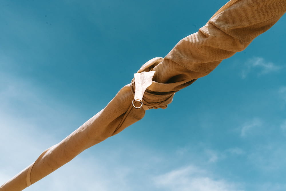 Twisted beige shade sail with a metal ring stretched diagonally across a blue sky