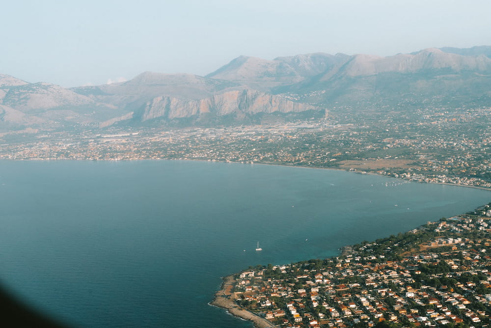 Aerial view of a wide bay, a coastal town and bare mountains in haze, from a plane